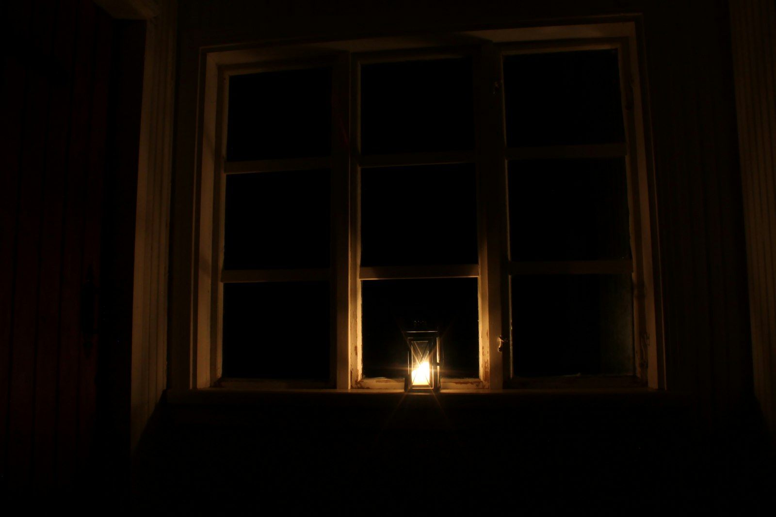 A candle burning on a windowsill in a dark room during a power outage